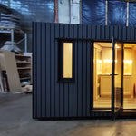 The Medium GlampTainer container-style glamping structure – left side front view with open glass door revealing softly lit kitchenette interior.