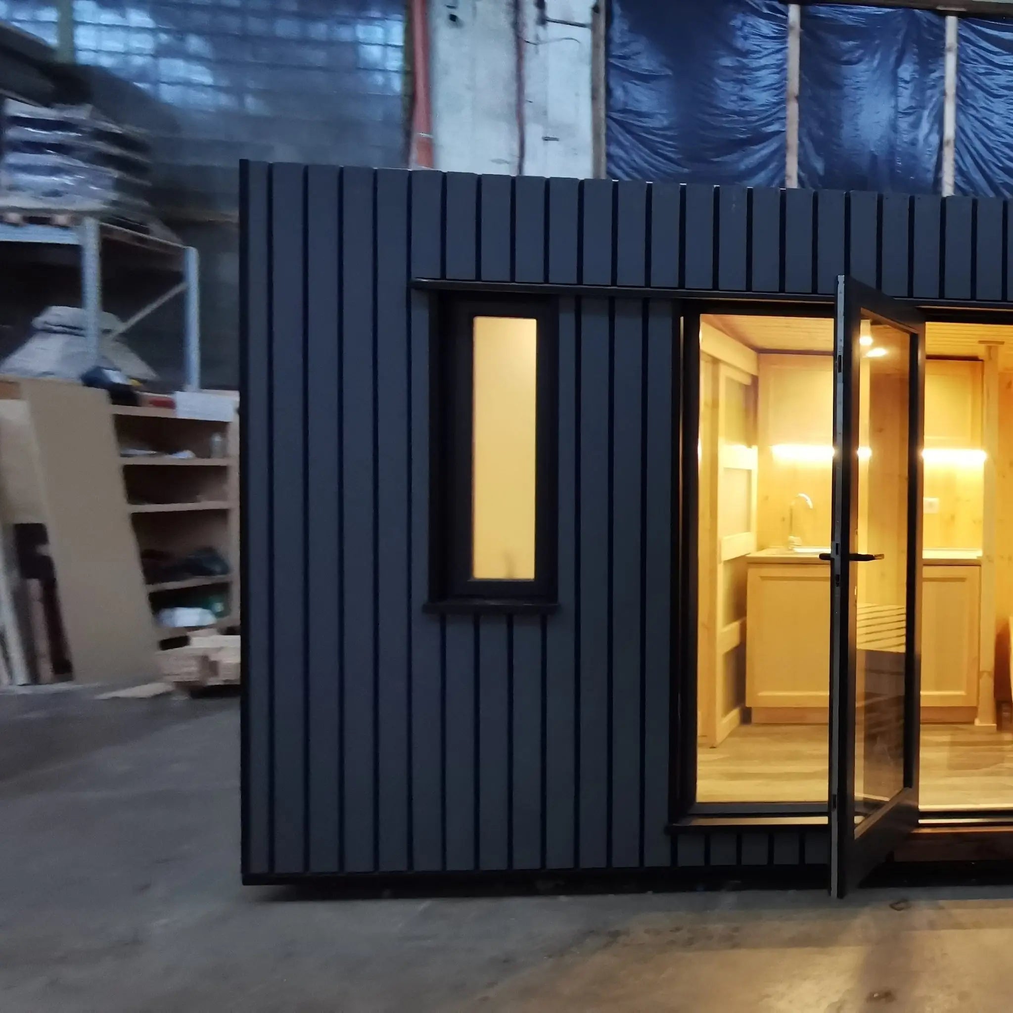 The Medium GlampTainer container-style glamping structure – left side front view with open glass door revealing softly lit kitchenette interior.