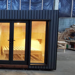 The Medium GlampTainer container-style glamping structure – right side front view with black-framed glass doors and warm glowing bedroom lighting.