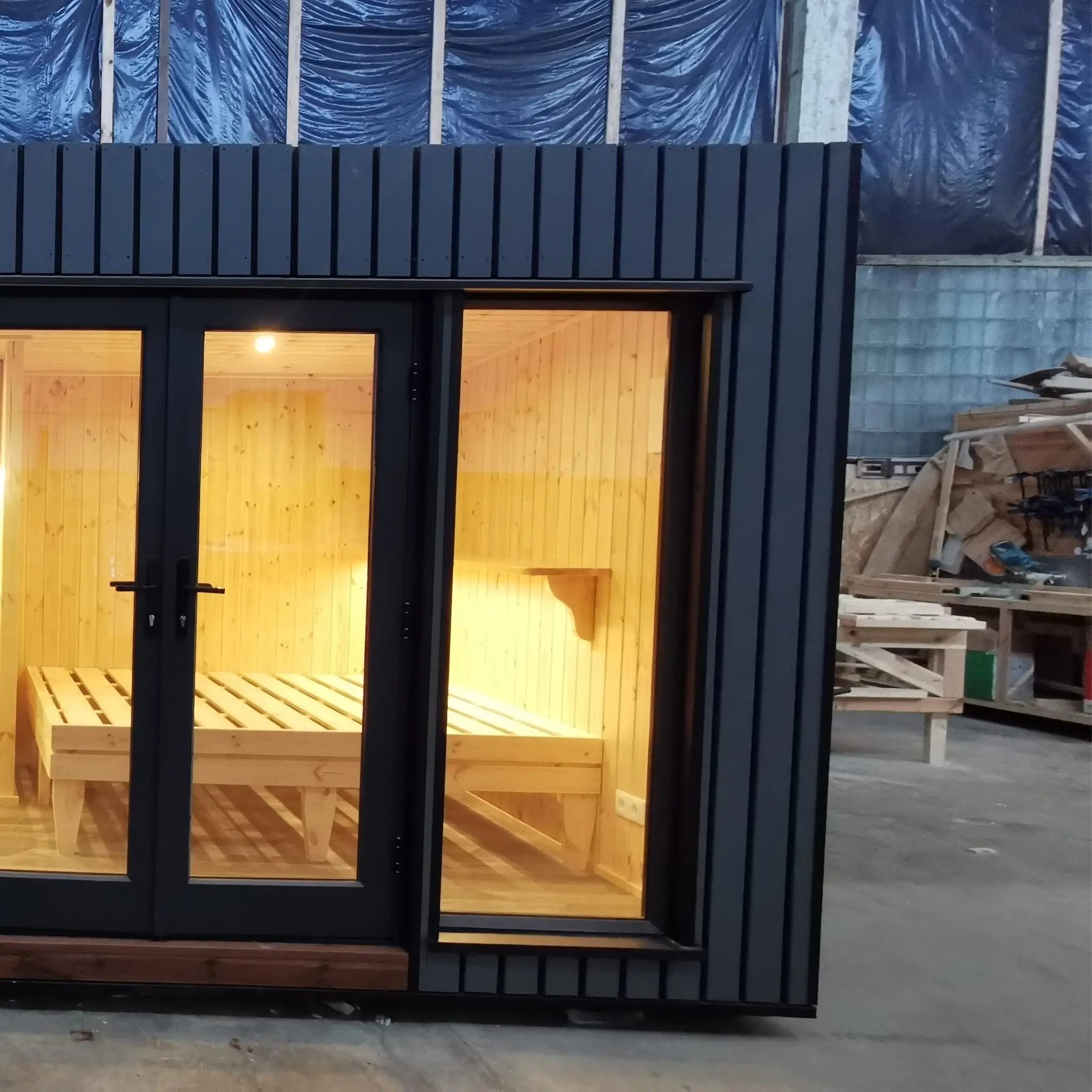 The Medium GlampTainer container-style glamping structure – right side front view with black-framed glass doors and warm glowing bedroom lighting.