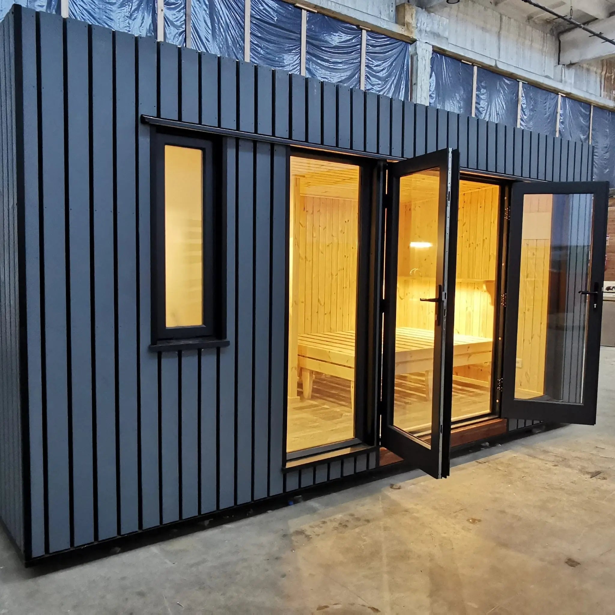 The Medium GlampTainer container-style glamping structure – angled side view showing sleek dark cladding and glass double doors opening to bedroom.