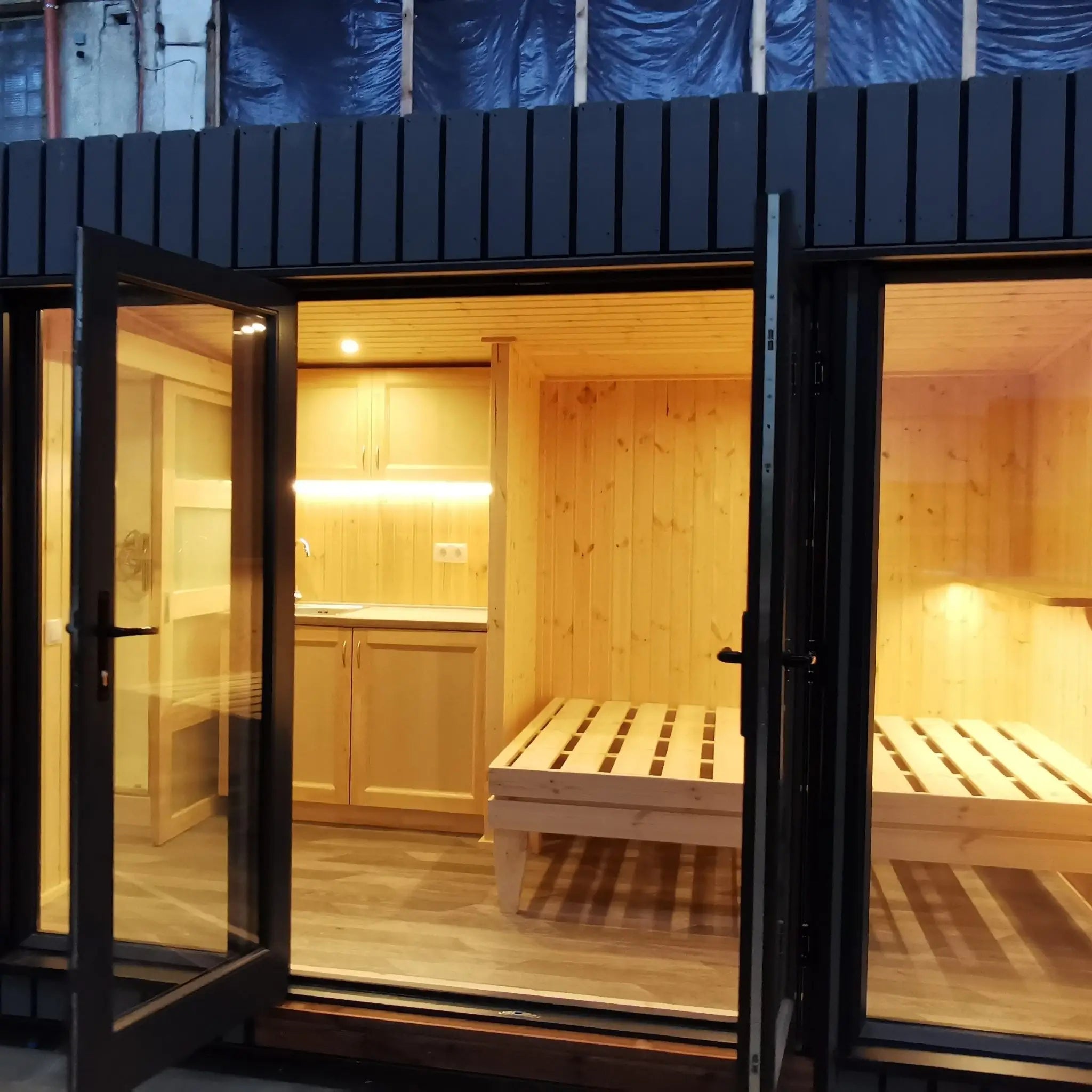 The Medium GlampTainer container-style glamping structure – view from entrance showing timber-lined bedroom with bed frame and warm ambient lighting.