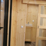 Compact bathroom entry inside The Medium GlampTainer container-style glamping structure – natural wood panelling with white ceramic basin.