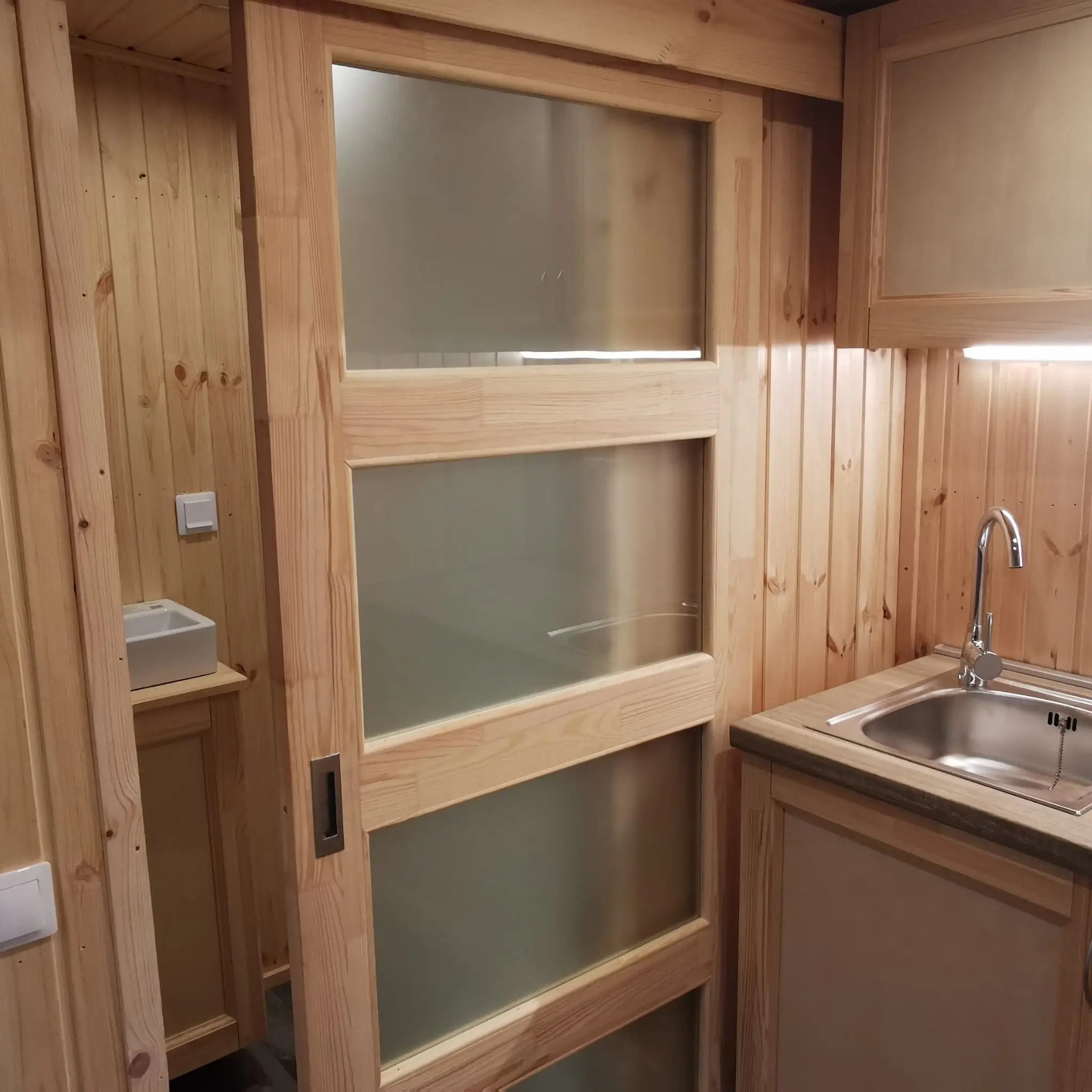 The Medium GlampTainer container-style glamping structure – interior view showing kitchenette, sliding door, and shower bathroom.