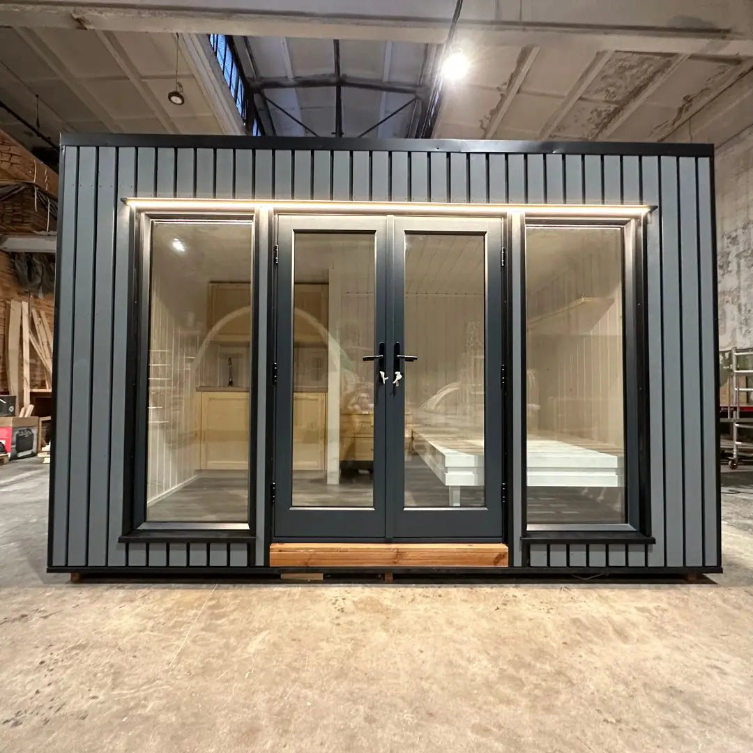 The Small GlampTainer container-style glamping structure – front exterior view with full-height glass doors, warm LED trim lighting, and a sleek architectural look.