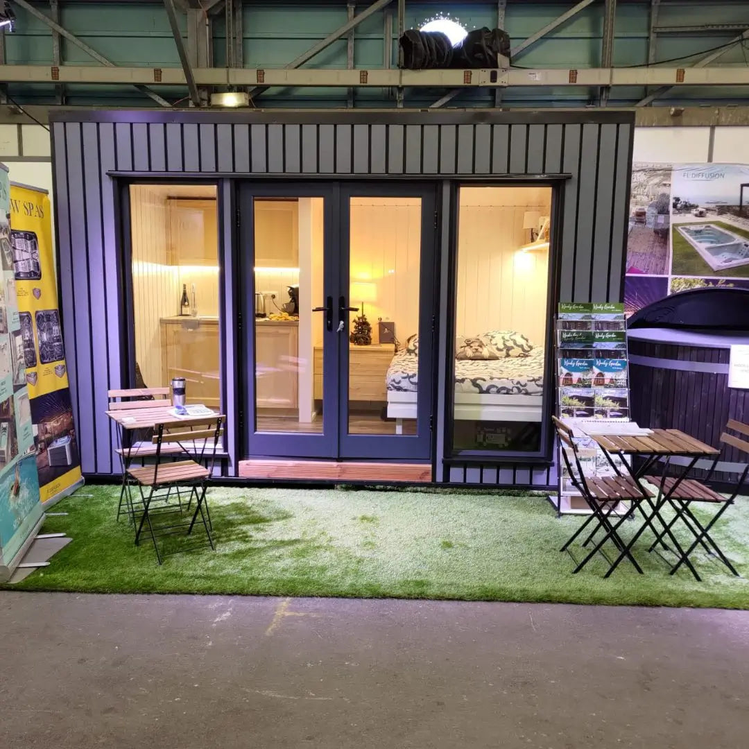 Fully furnished Small GlampTainer container-style glamping structure – illuminated front view featuring cosy bedroom, kitchenette, and outdoor seating setup.