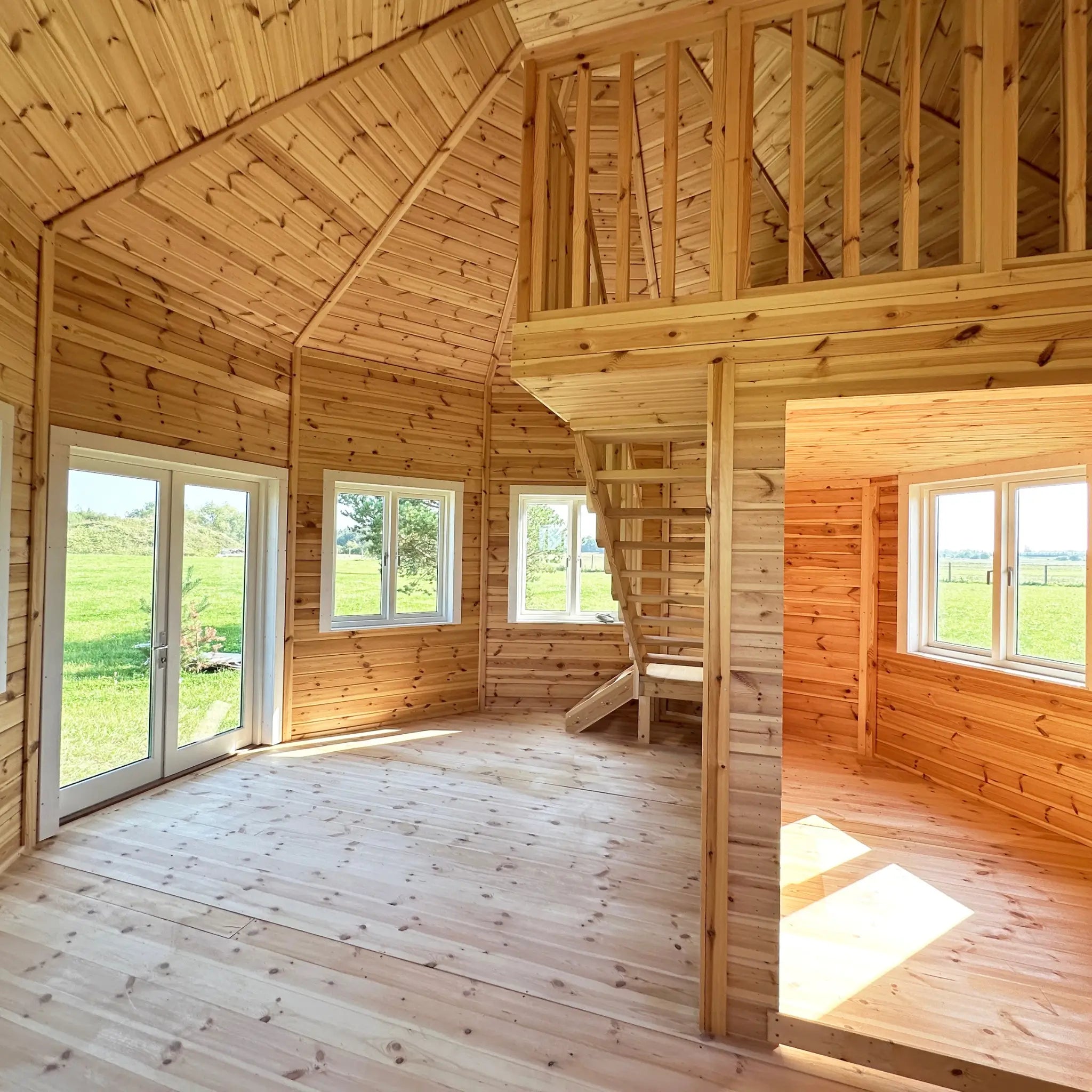 Interior view showing loft platform with timber balustrade above the enclosed ground-floor room in the Altura Loft Cabin