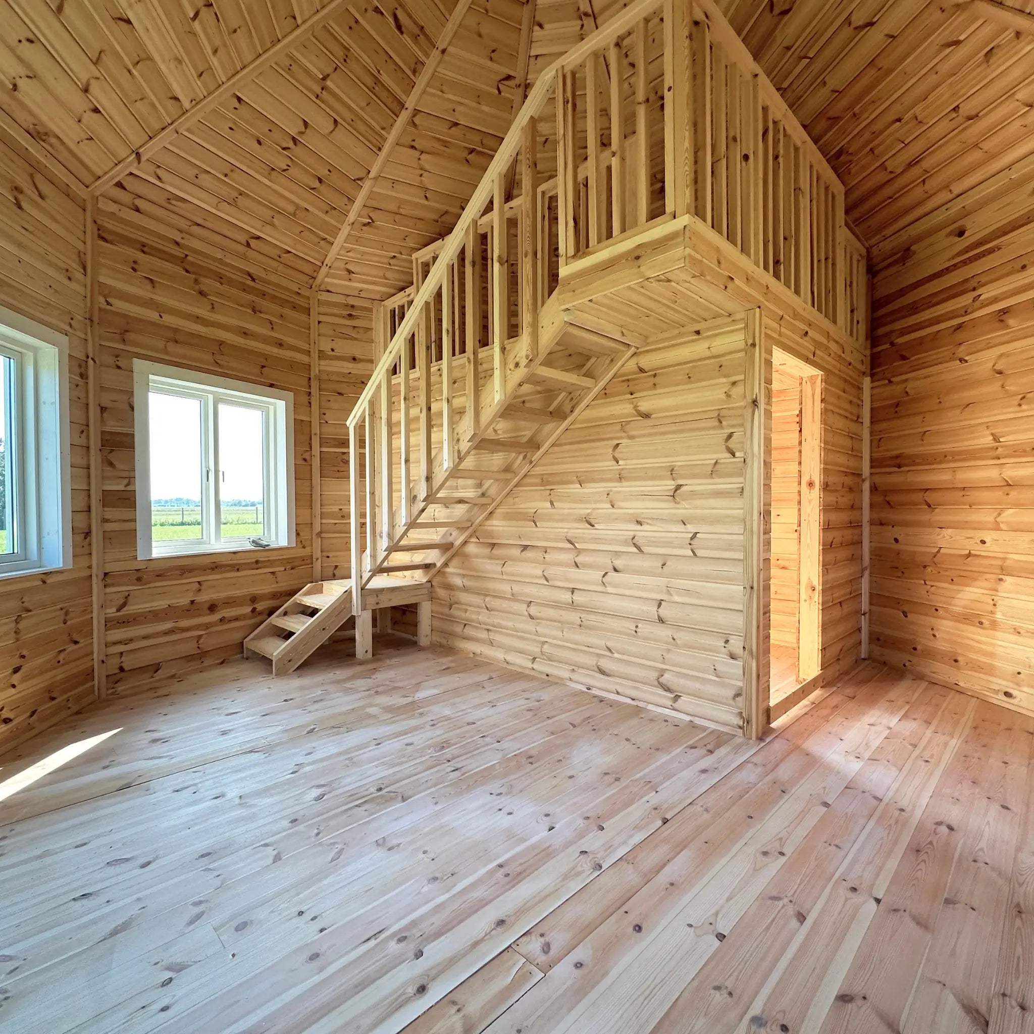 Open-plan ground floor interior of the Altura Loft Cabin featuring timber flooring, staircase, and loft platform above