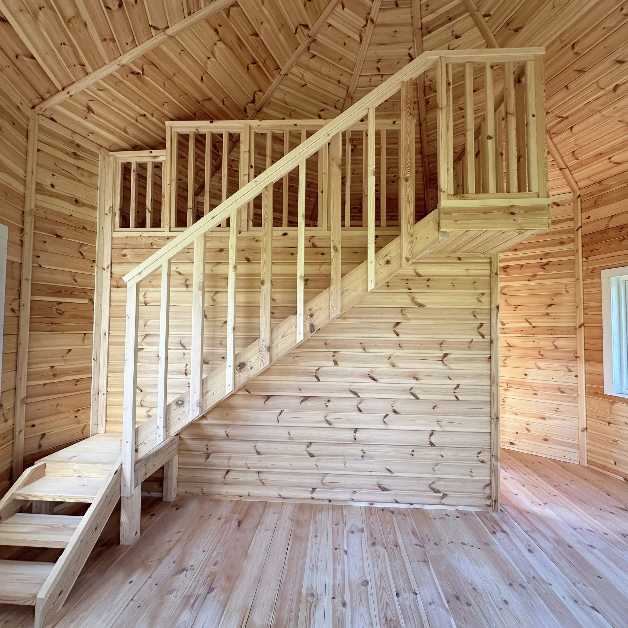 Open-plan interior of the Altura Loft Cabin showing timber staircase, mezzanine balustrade, and vaulted ceiling