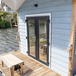 Close-up of floating shepherd’s hut entrance with double glass doors and timber deck beside the water.