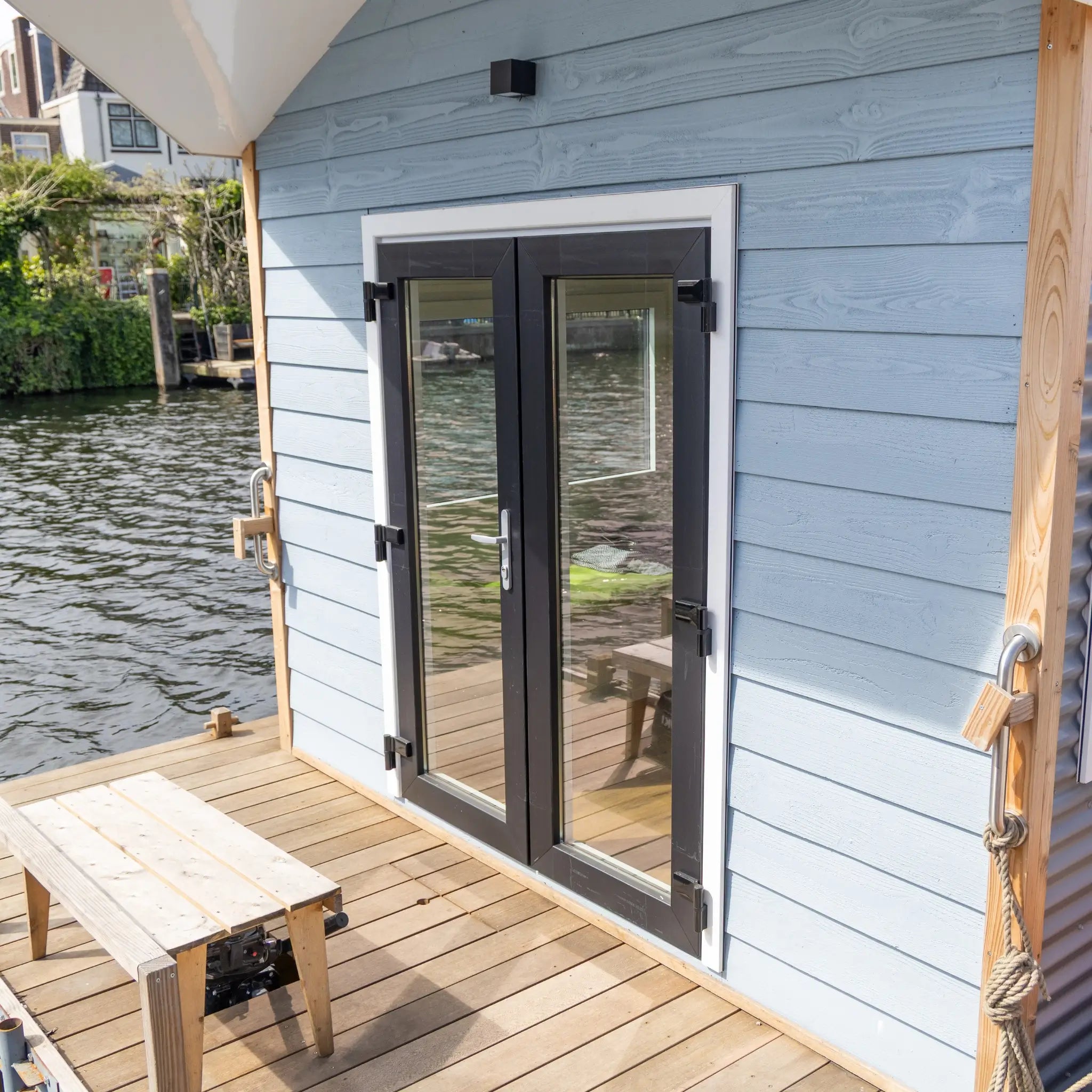 Close-up of floating shepherd’s hut entrance with double glass doors and timber deck beside the water.