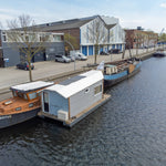 Rear side view of a compact floating shepherd’s hut with modern cabin design and canal surroundings.