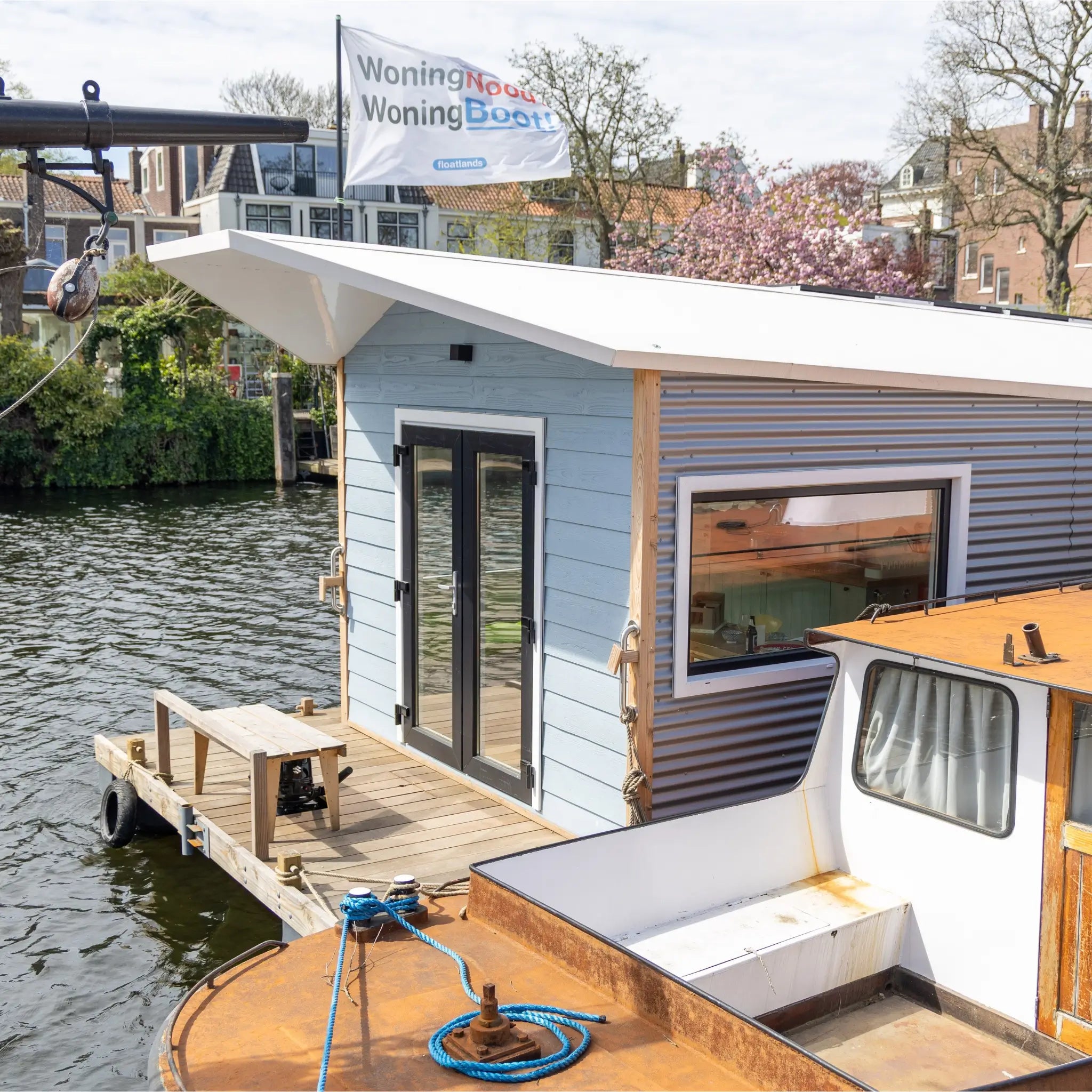 Exterior side close-up of a floating shepherd’s hut with waterside deck, large windows and floating platform.