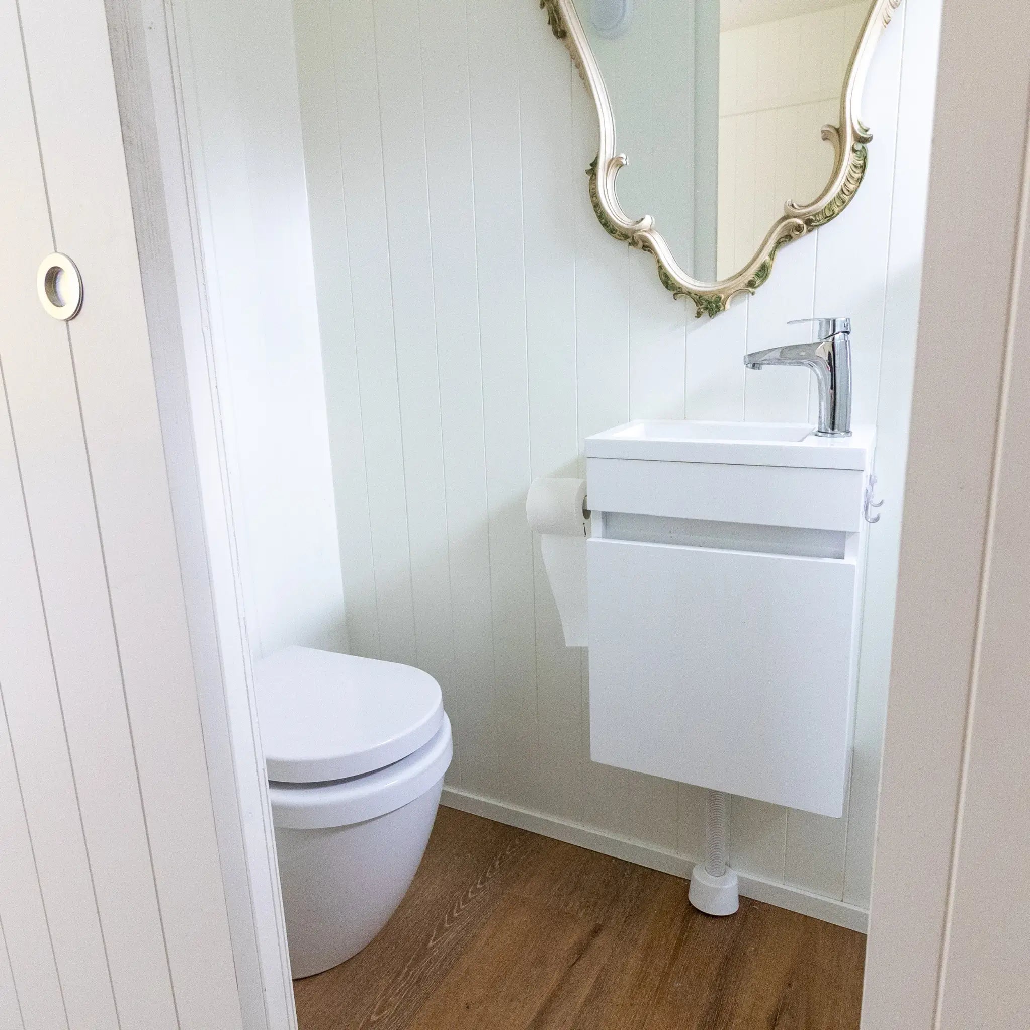 Compact bathroom inside a floating shepherd’s hut with toilet, vanity unit and decorative mirror.