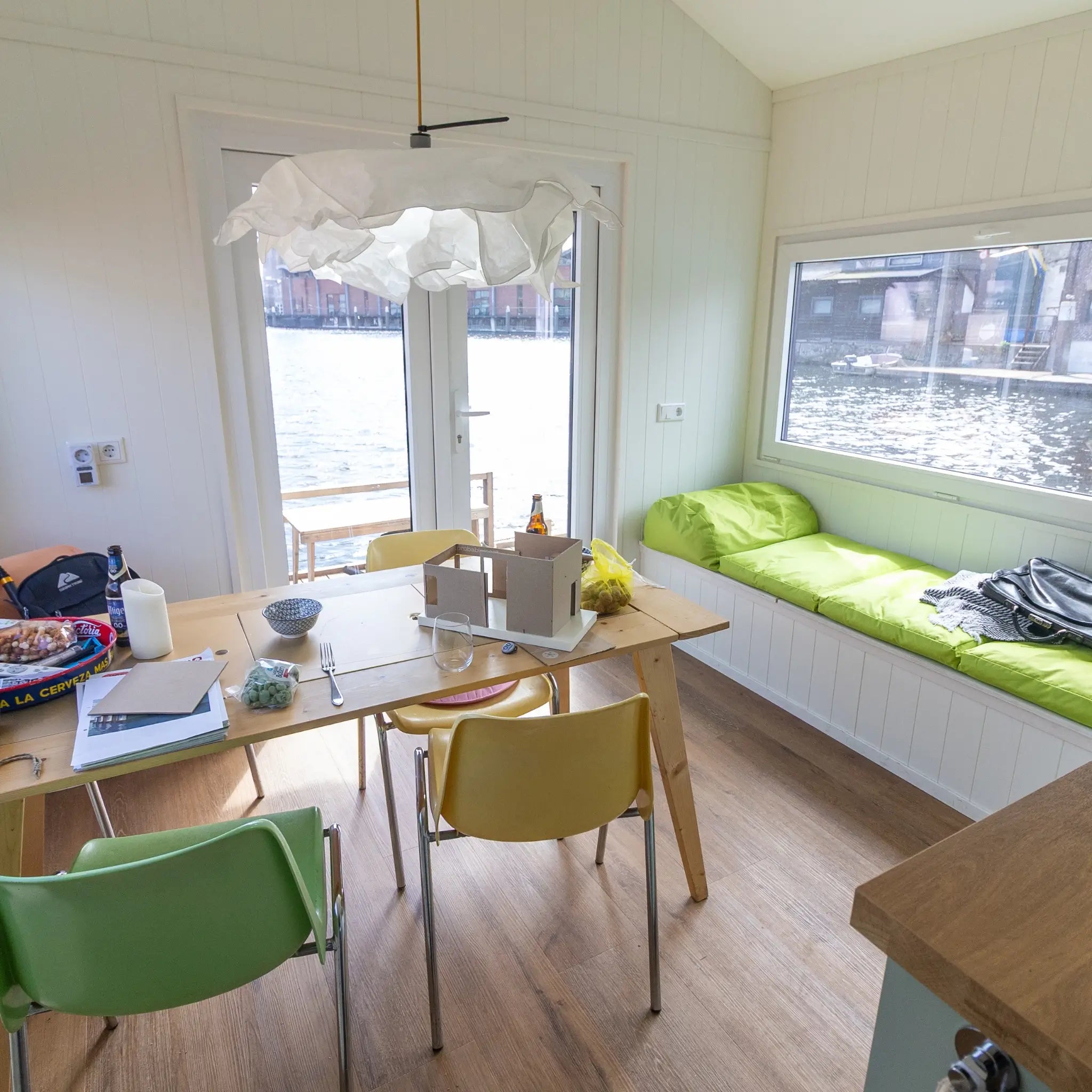 Bright dining area inside a floating shepherd’s hut featuring built-in window seating and waterside views.