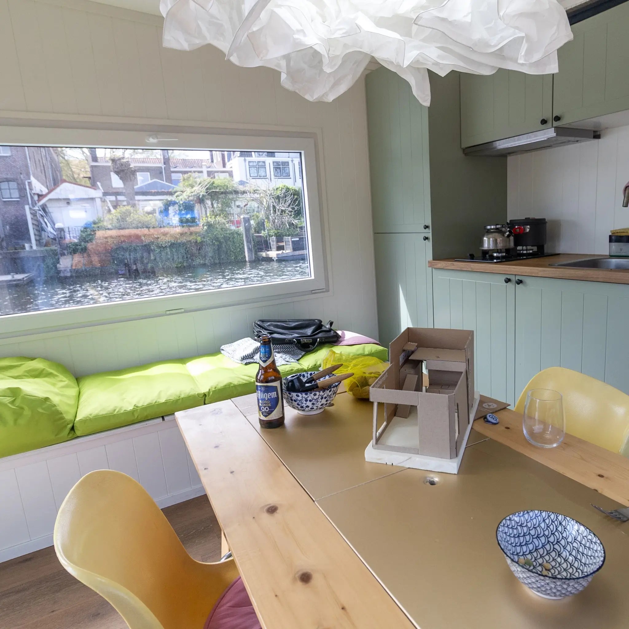 Dining area and window bench inside a floating shepherd’s hut with panoramic canal views and compact kitchen.