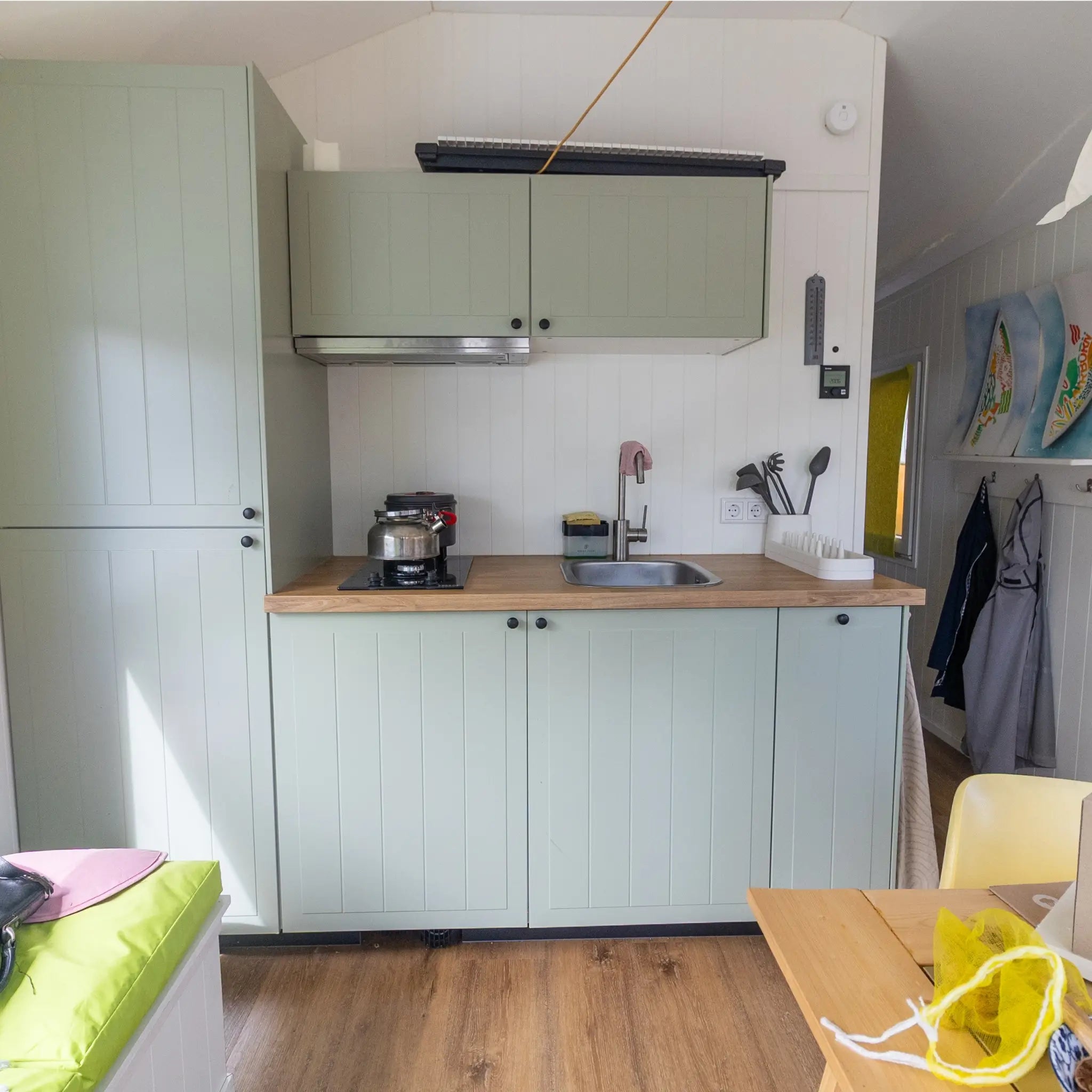 Compact kitchen interior with sage green cabinetry, wood countertops and minimalist floating tiny home styling.