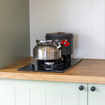 Compact gas hob with kettle and cookware inside a modern floating tiny home kitchen.