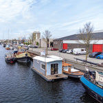 Front view of a modern floating shepherd’s hut moored along an urban canal marina.