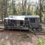 Front exterior view of a modern 2 person shepherd’s hut surrounded by peaceful woodland scenery and private outdoor terrace.