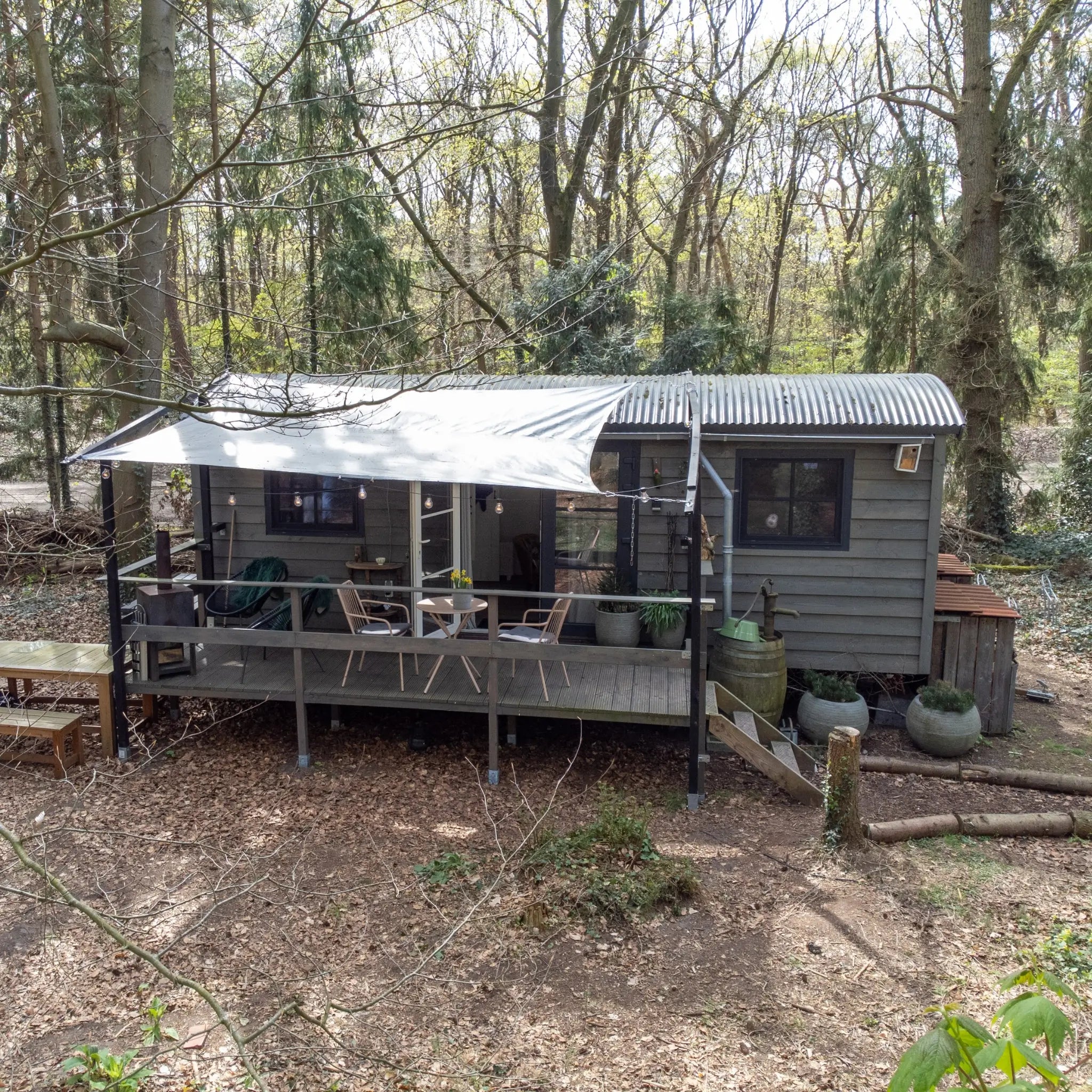 Front exterior view of a modern 2 person shepherd’s hut surrounded by peaceful woodland scenery and private outdoor terrace.