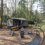 Woodland glamping shepherd’s hut with outdoor firepit seating area and peaceful forest escape setting.