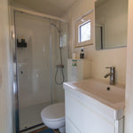 Modern shepherd’s hut bathroom with walk-in shower, compact vanity unit and bright minimalist interior design.