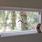 Shepherd’s hut bedroom window with woodland views and decorative stained glass bird detail.