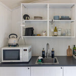 Compact shepherd’s hut kitchen counter with open shelving, sink area and modern self-catering essentials.