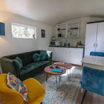 Contemporary shepherd’s hut living area with velvet sofa, kitchenette and cosy woodland cabin interior.