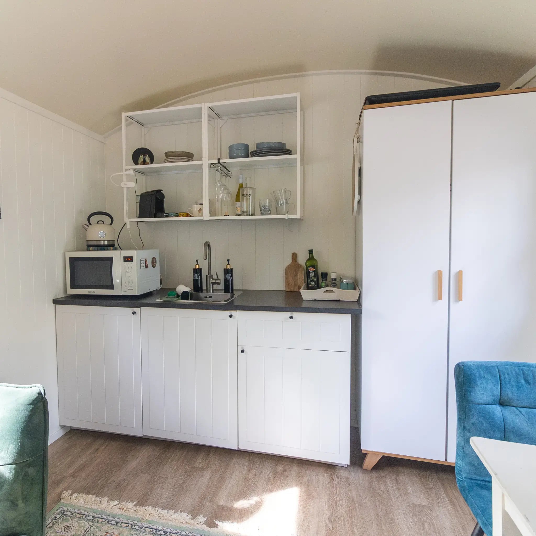 Minimalist kitchenette inside a luxury shepherd’s hut with open shelving, compact appliances and modern design.