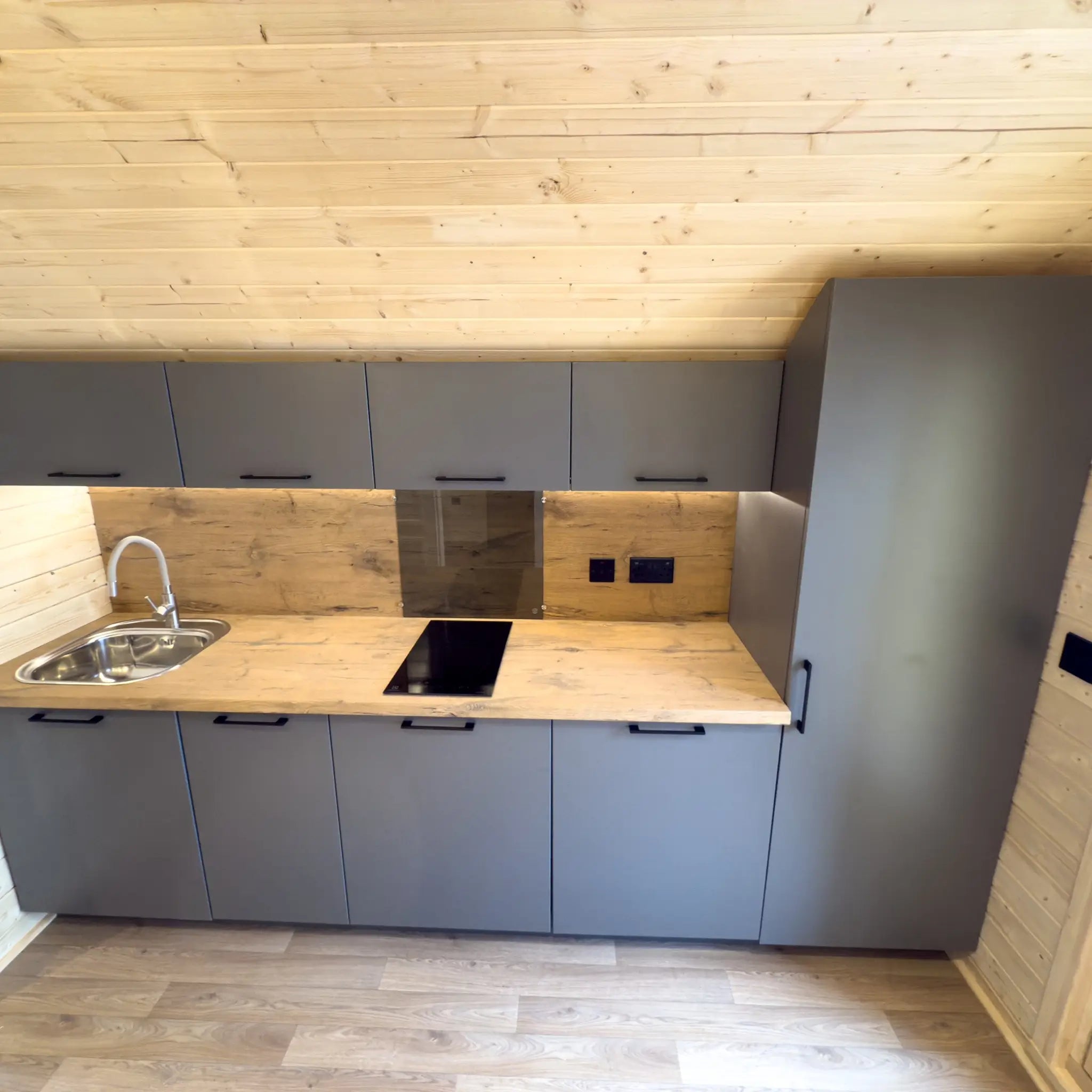 Modern kitchenette inside the Dual Halfmoon glamping pod with grey cabinets and wooden countertop