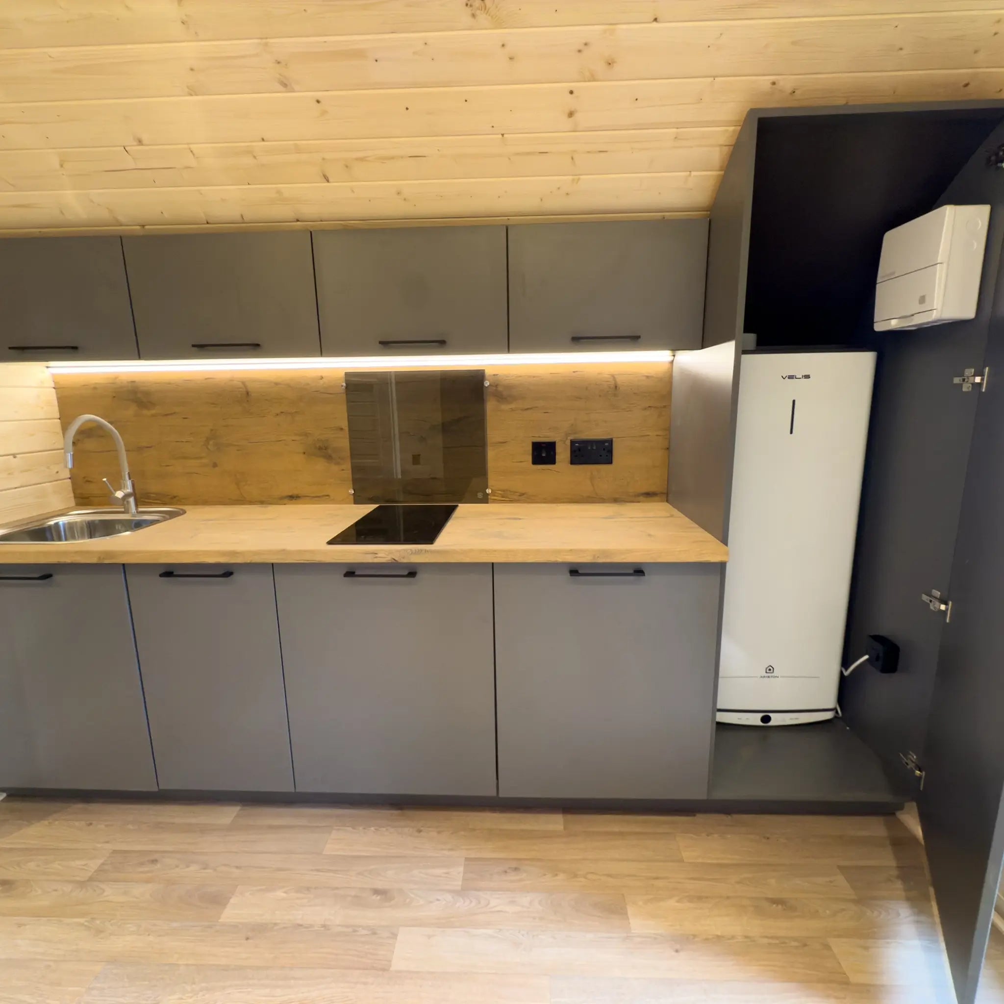 Wide interior view of the kitchen area with grey storage units and timber wall panels
