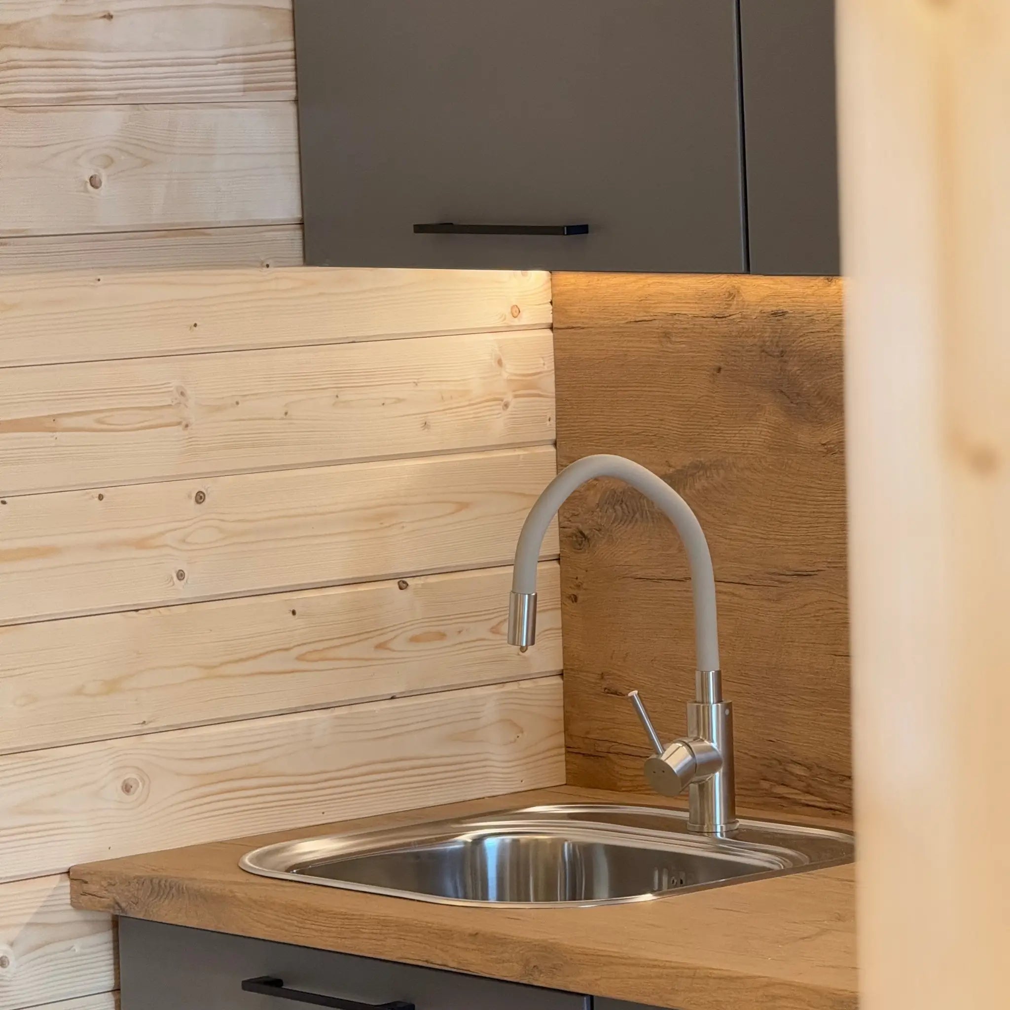 Close-up of modern kitchen tap and sink installed in the wooden countertop inside the glamping pod