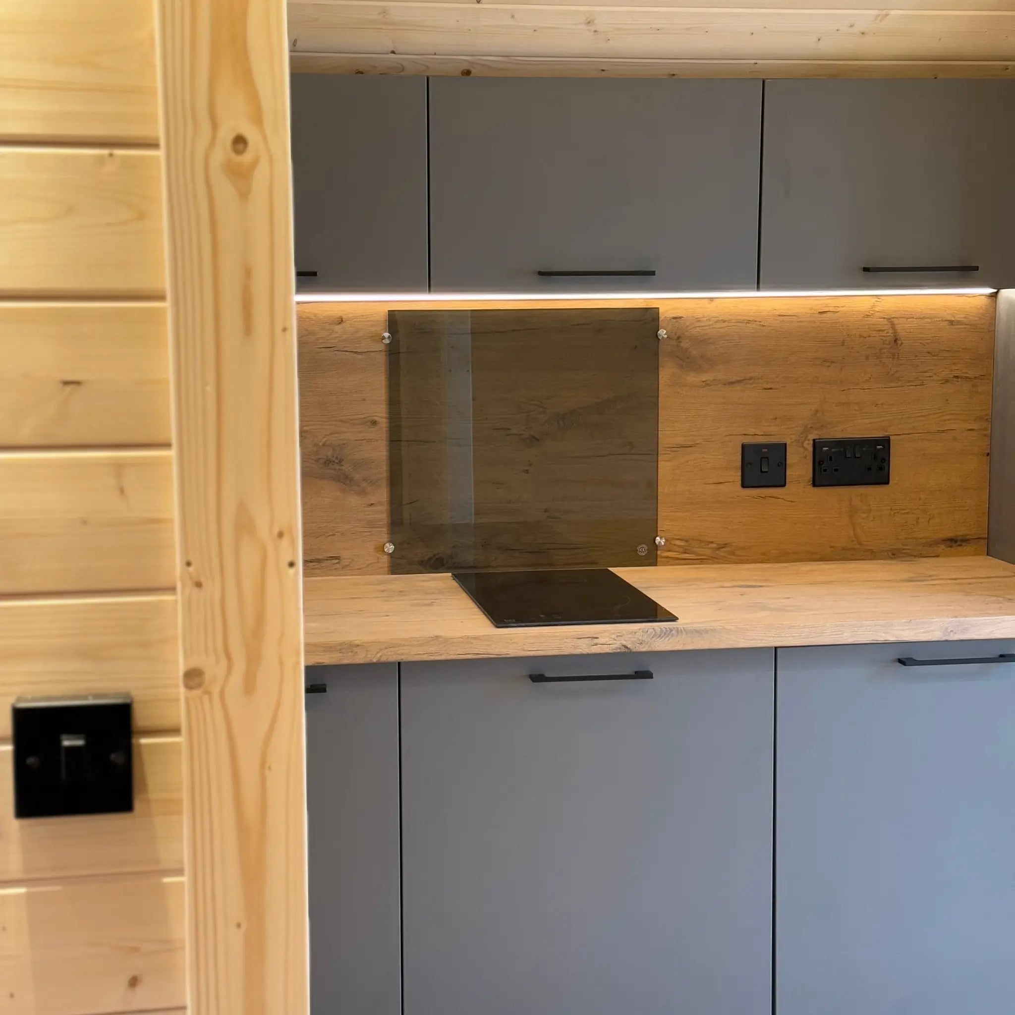 Compact kitchenette inside the Dual Halfmoon 2 person glamping pod with grey cabinets, wooden worktop and induction hob