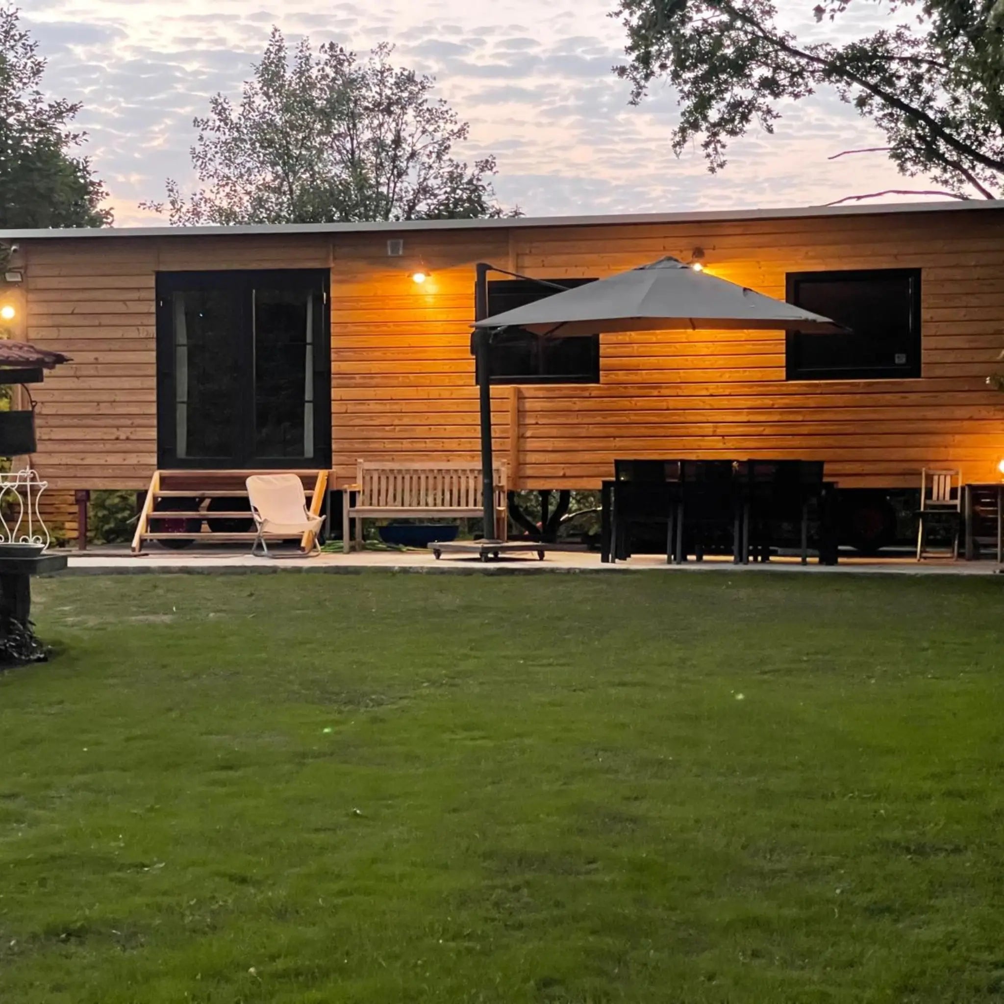 Timber-clad exterior of The Elmstead 2 Person Shepherd’s Hut with outdoor dining area and warm exterior lighting