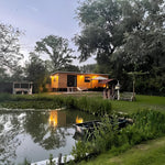 The Elmstead 2 Person Shepherd’s Hut beside a landscaped pond in a peaceful countryside setting