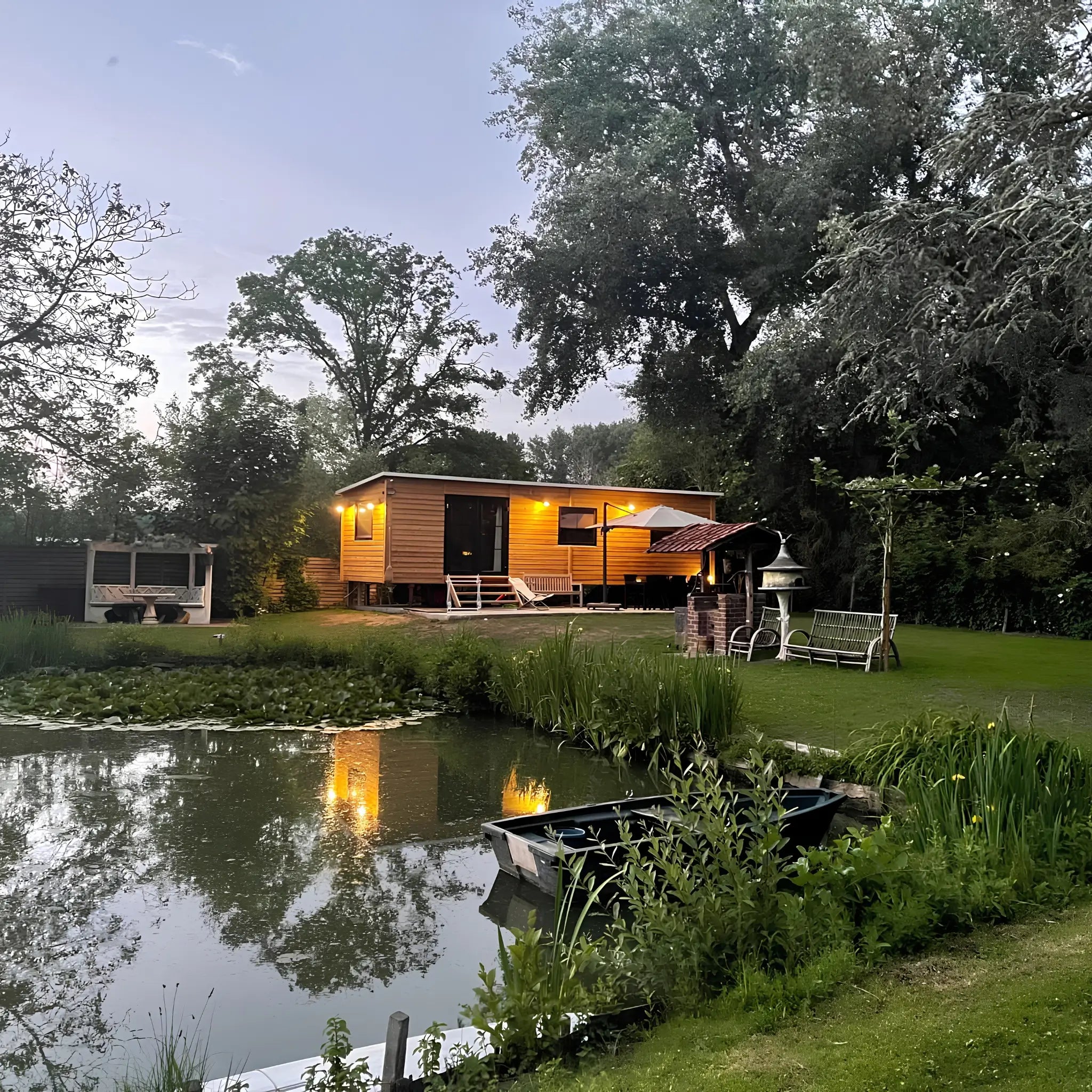The Elmstead 2 Person Shepherd’s Hut beside a landscaped pond in a peaceful countryside setting