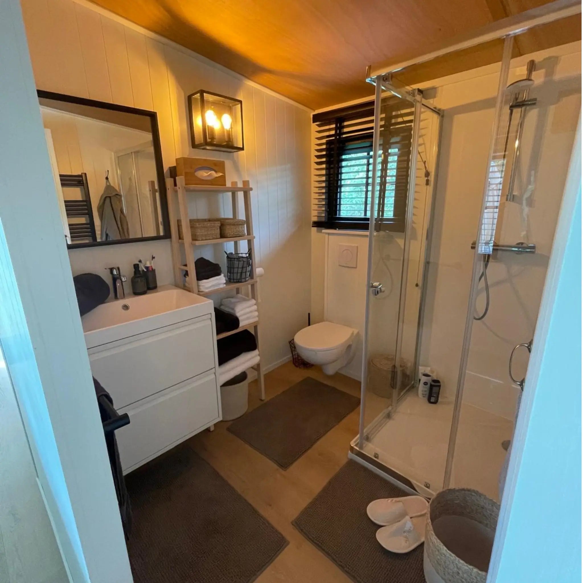 Modern bathroom inside The Elmstead 2 Person Shepherd’s Hut with shower enclosure, toilet, vanity and timber ceiling