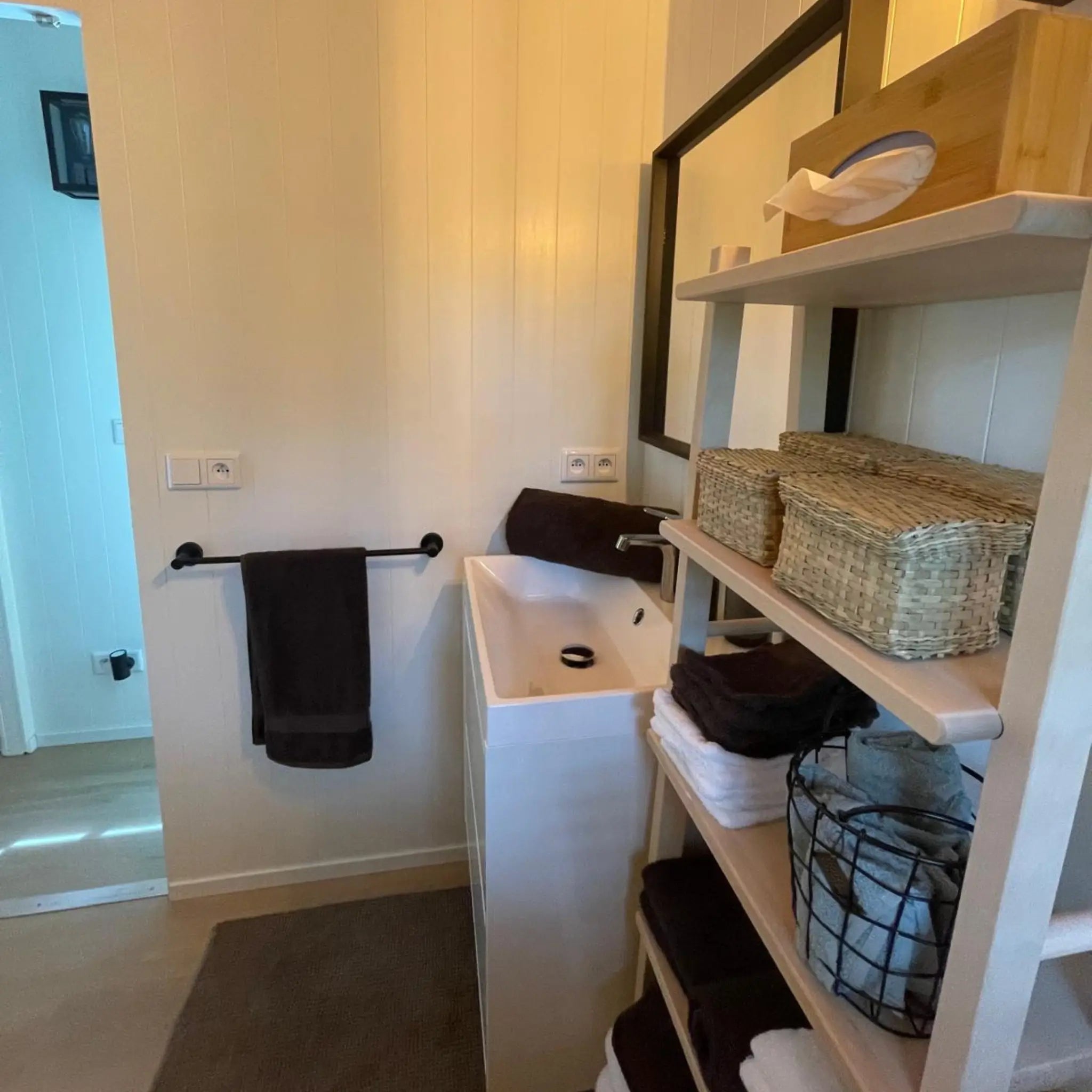 Bathroom vanity and storage inside The Elmstead 2 Person Shepherd’s Hut with timber shelving and black-framed mirror