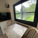Dining area inside The Elmstead 2 Person Shepherd’s Hut with table, wooden chairs and pond views through a large window