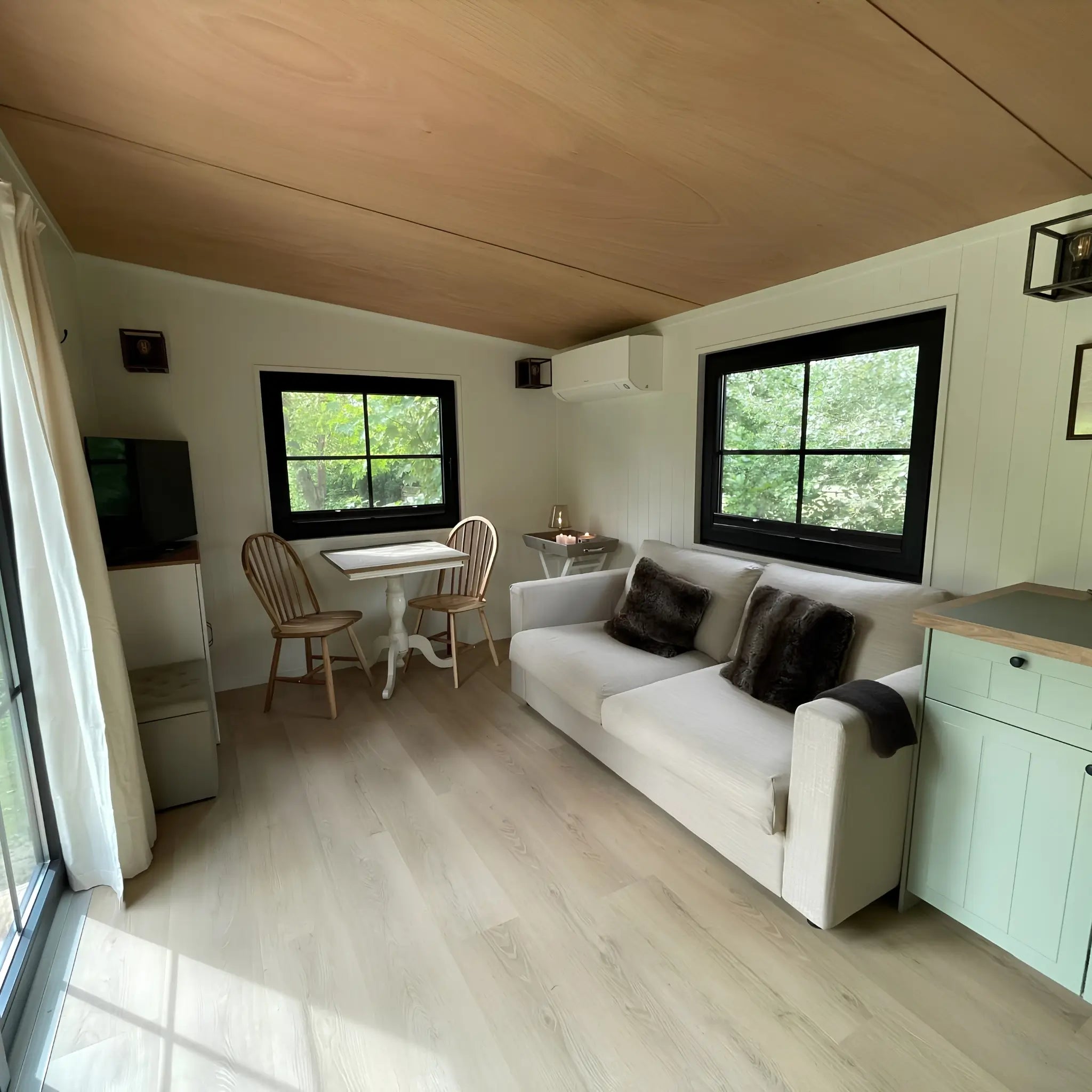 Open-plan living area in The Elmstead 2 Person Shepherd’s Hut with sofa, dining table, kitchen and large black-framed windows