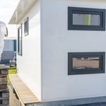 Rear exterior view of modern floating shepherd’s hut with white cladding, slimline windows, and timber side decking.
