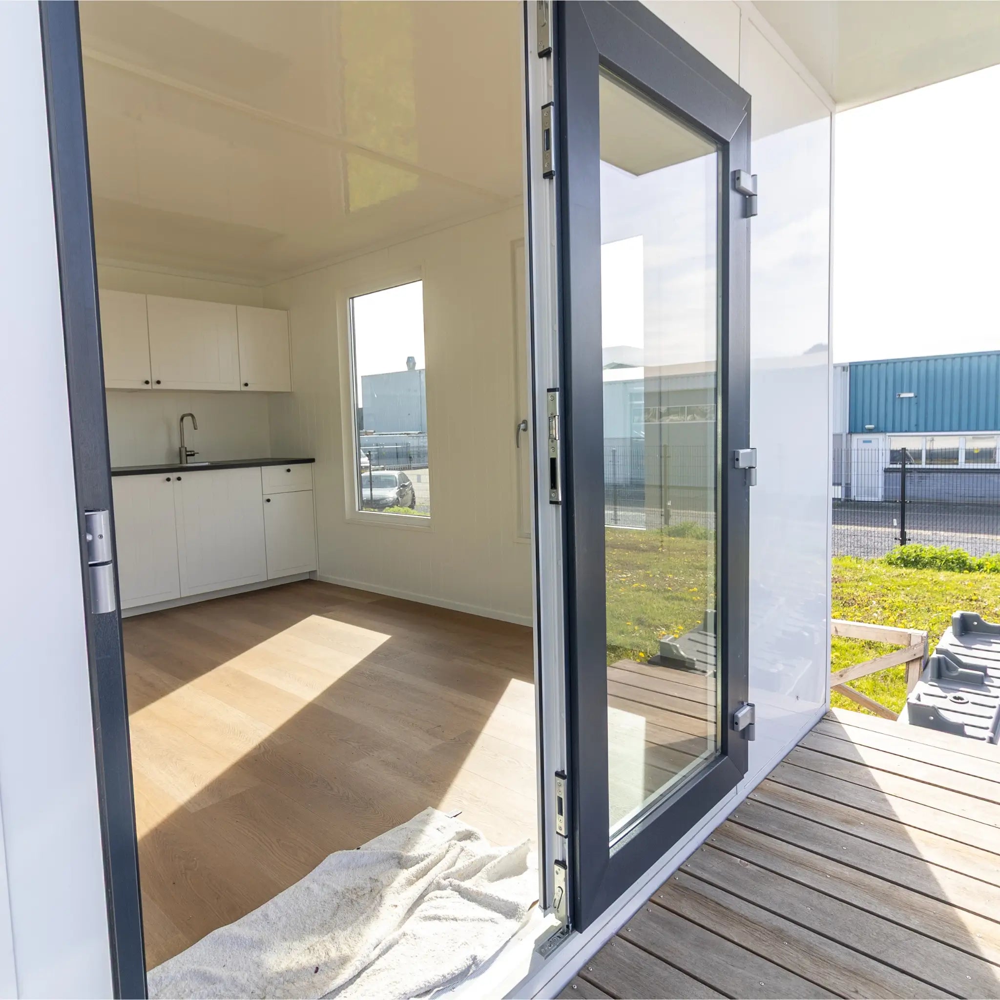 Entrance view of floating shepherd’s hut with glazed patio doors, timber decking, and bright open-plan interior.