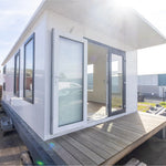 Close-up front exterior of modern floating shepherd’s hut with covered decking and large contemporary glass doors.