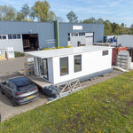 Side exterior view of compact floating shepherd’s hut with white cladding, tall modern windows, and minimalist design.