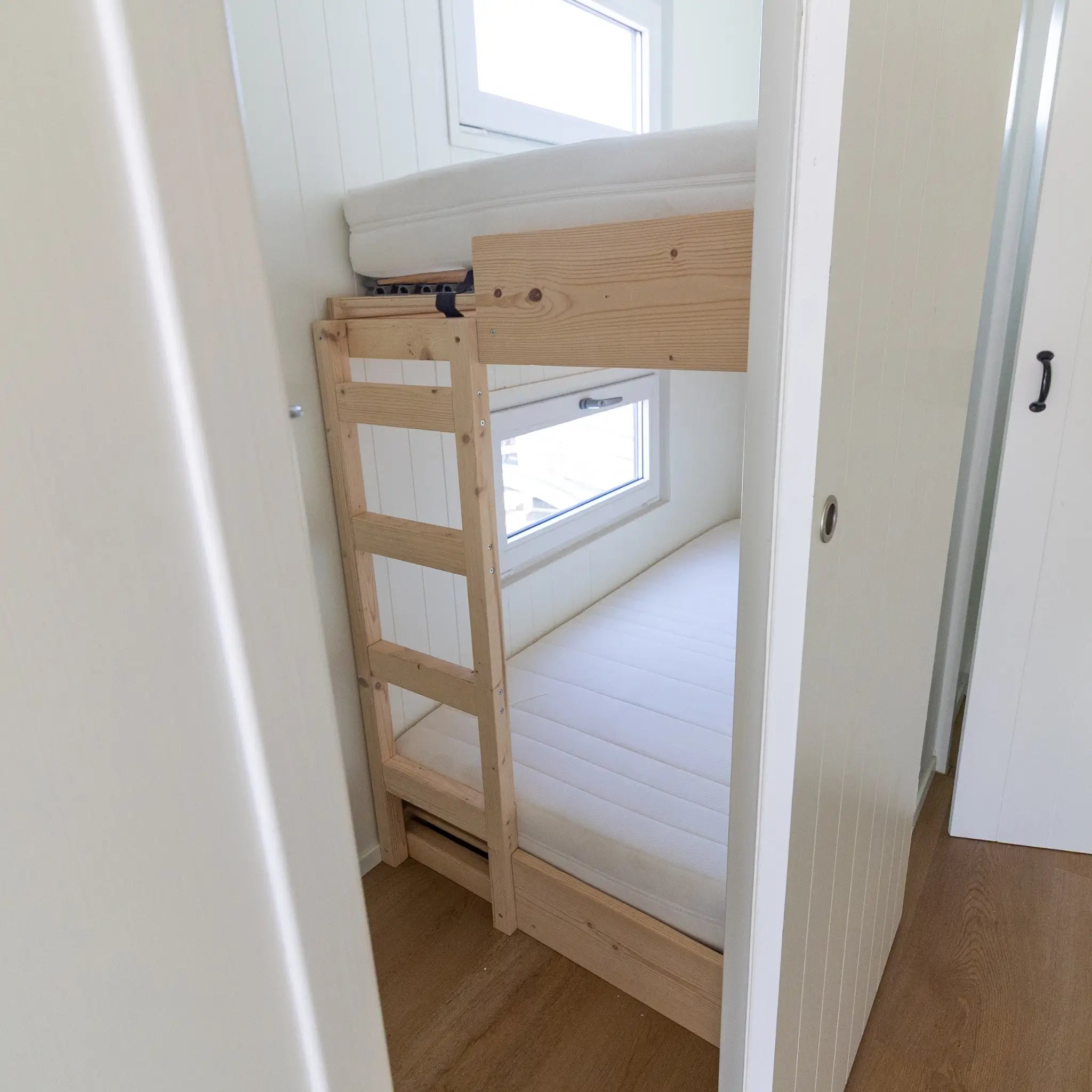 Compact bunk bed room with built-in wooden bunks, bright white interior, and modern minimalist styling.