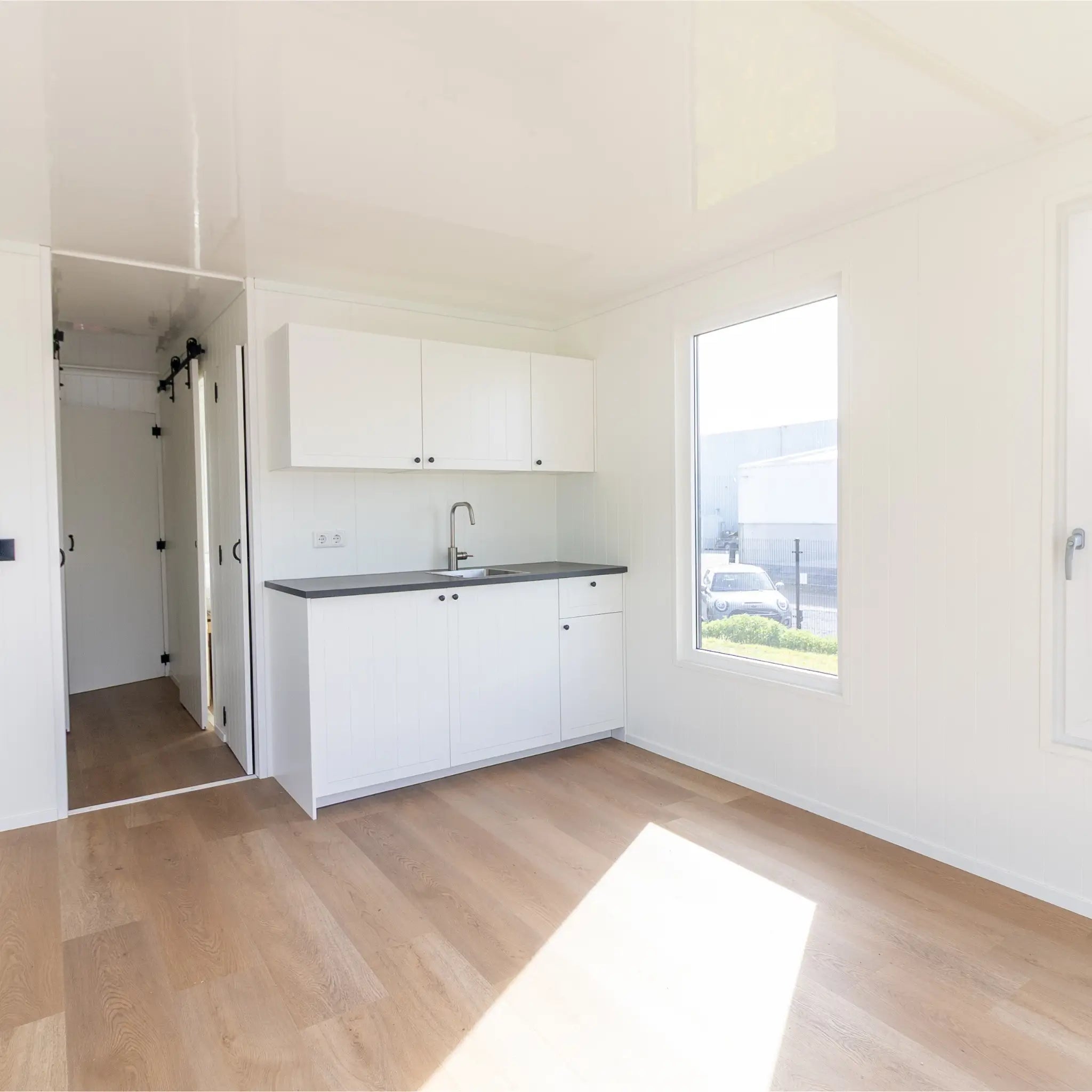 Open-plan interior with kitchenette, wood flooring, and bright minimalist floating shepherd’s hut design.