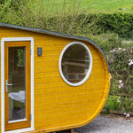 Front door and circular window of Grotto 3 berth glamping pod with contemporary wooden exterior