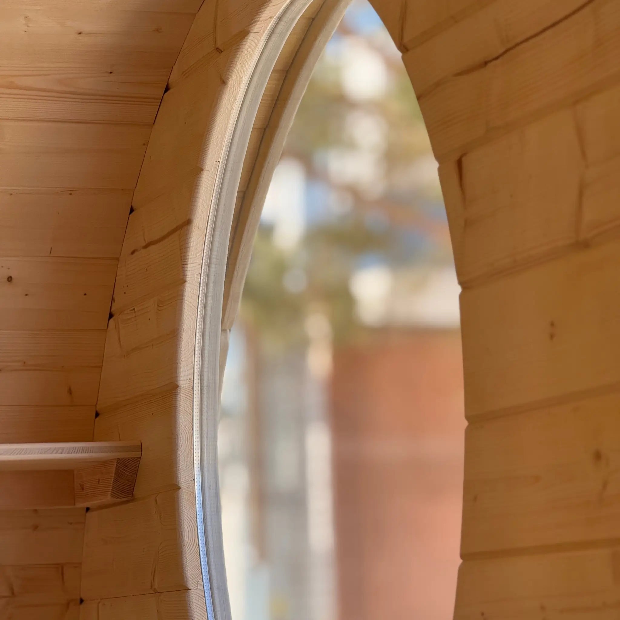 Interior view through circular window of Grotto glamping pod showing natural wood finish and cozy space